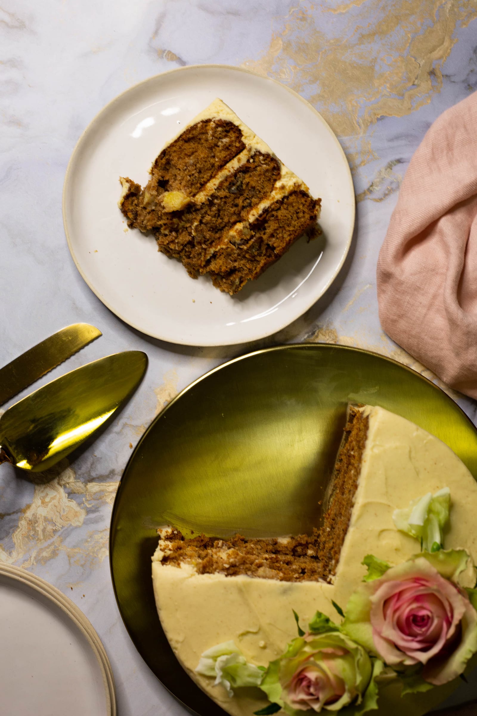 A slice of hummingbird cake on a white plate beside the cut cake and its roses, from above