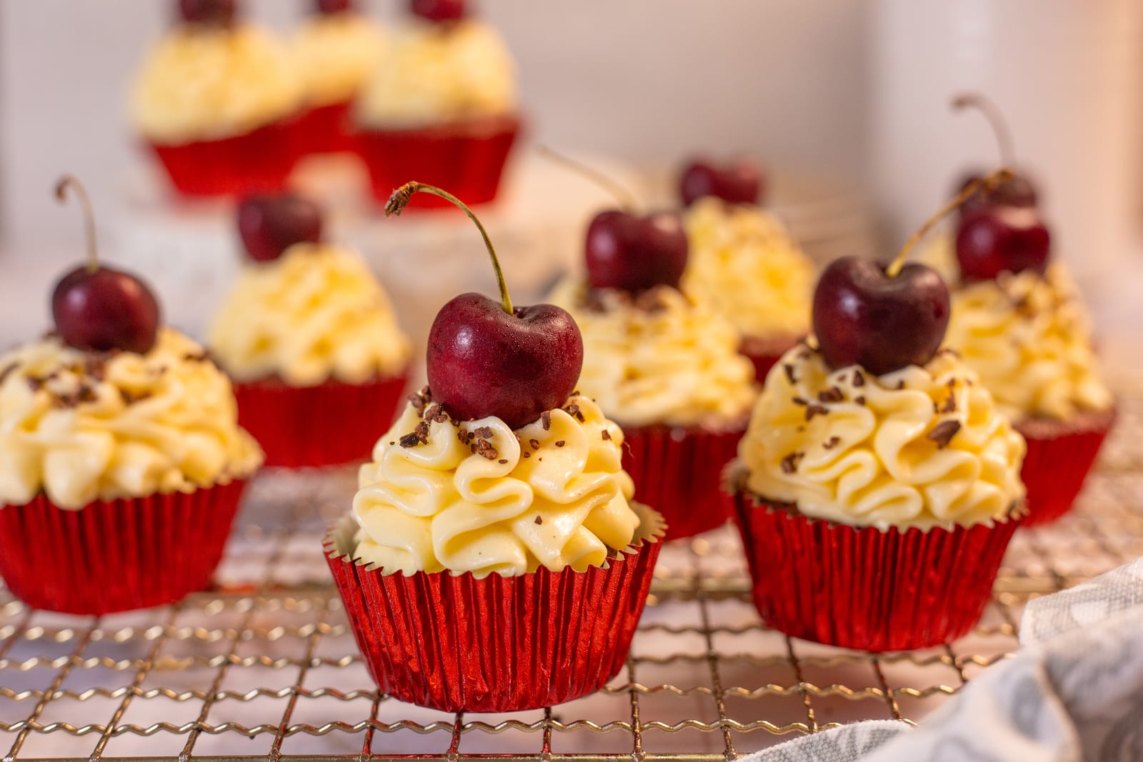 Red velvet cupcakes with cream cheese frosting and a cherry on top, on a wire rack