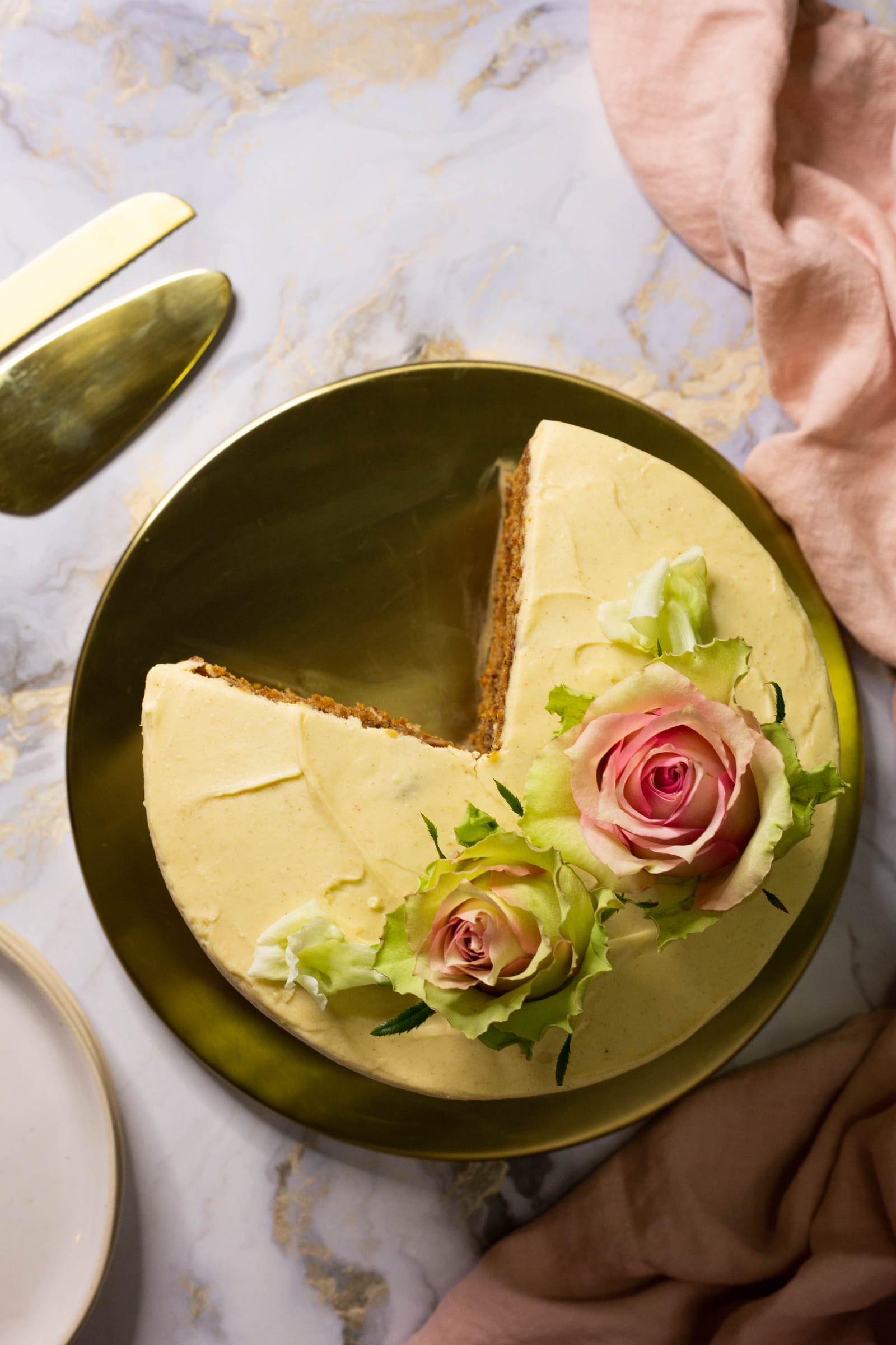 A hummingbird cake topped with pink and green roses on a gold board, a wedge cut out, from above