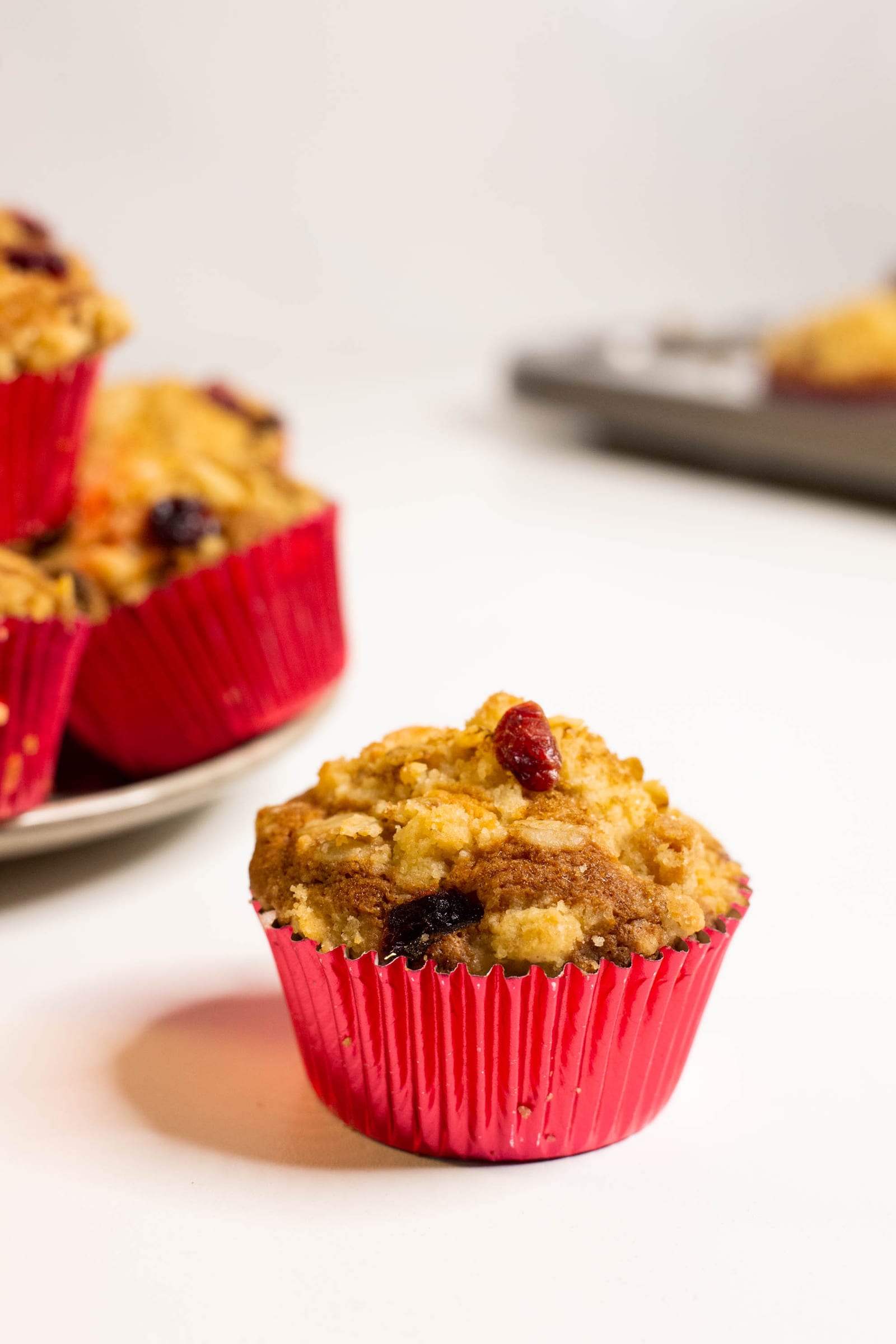 A single cranberry crumble muffin in a red case, the pile blurred behind