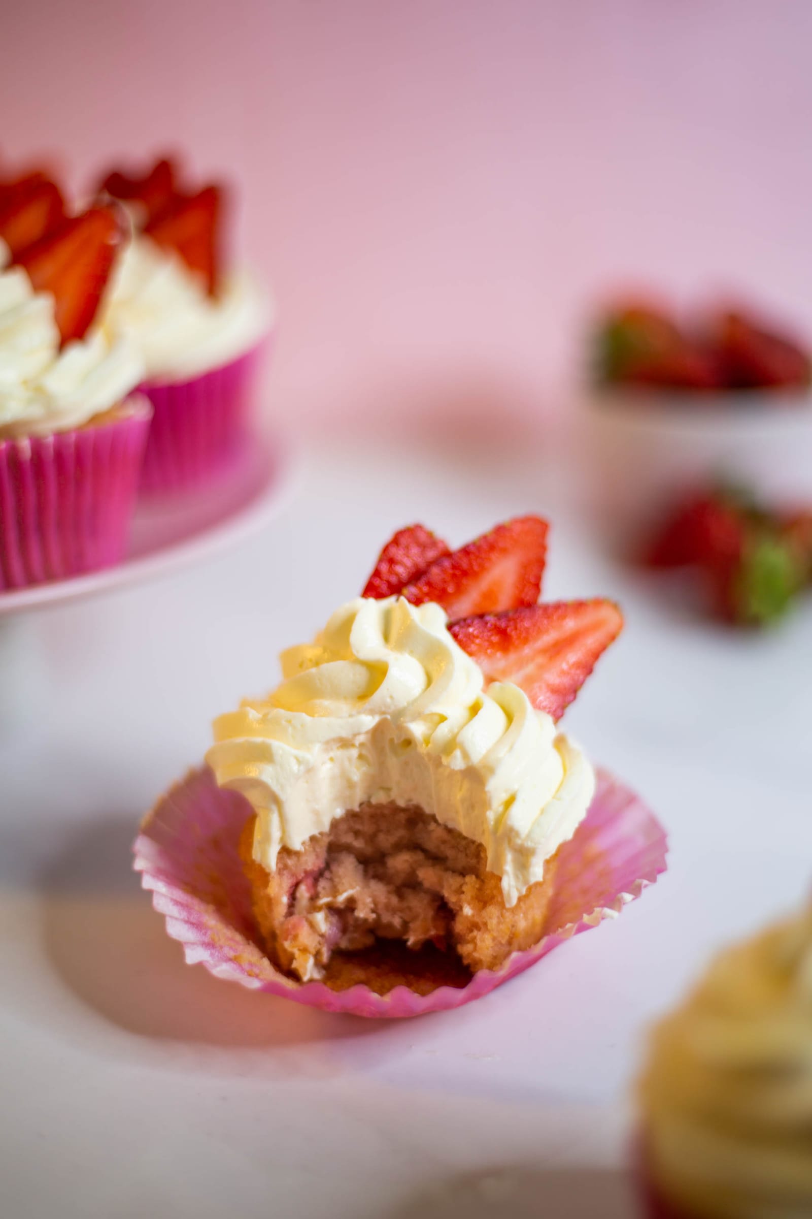 A bitten strawberry and white chocolate cupcake, showing the pink inside