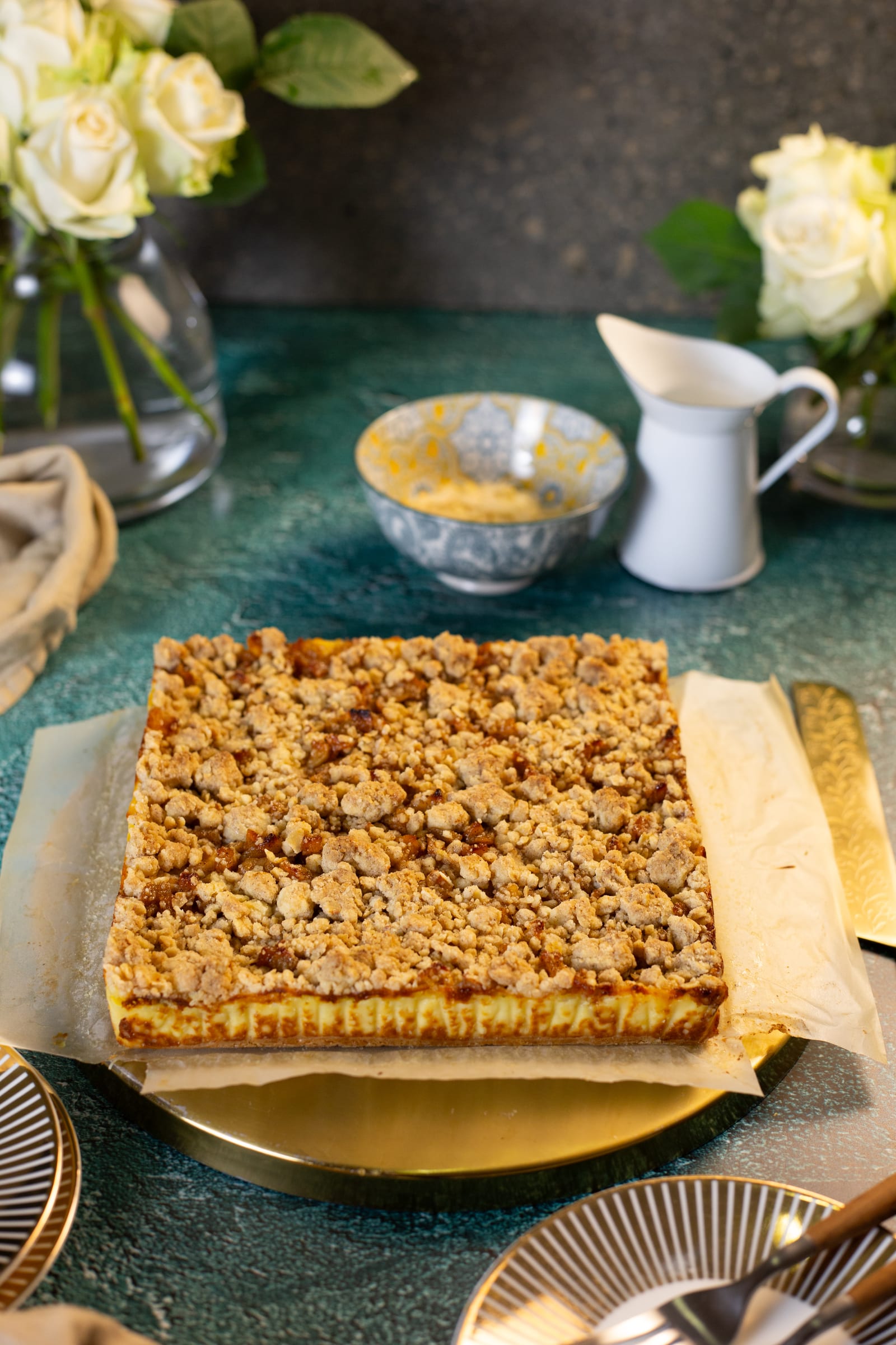A tray of milk tart crumble bars on a gold plate, with white roses and a milk jug