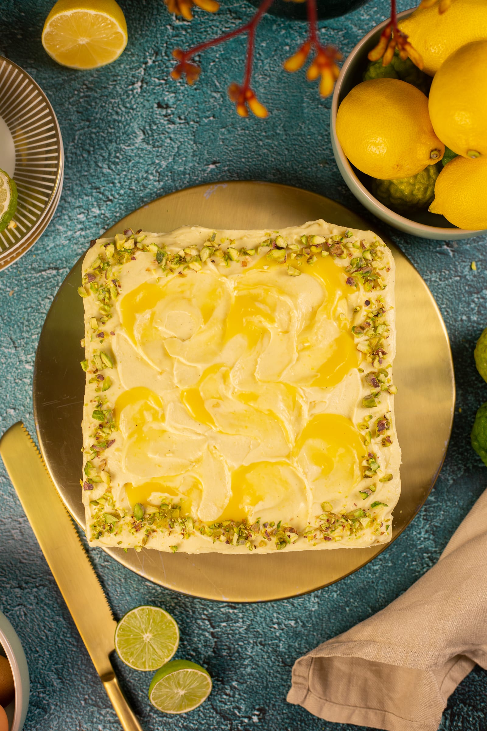 A pistachio and lemon traybake from above, topped with swirls of lemon curd and a chopped-pistachio border