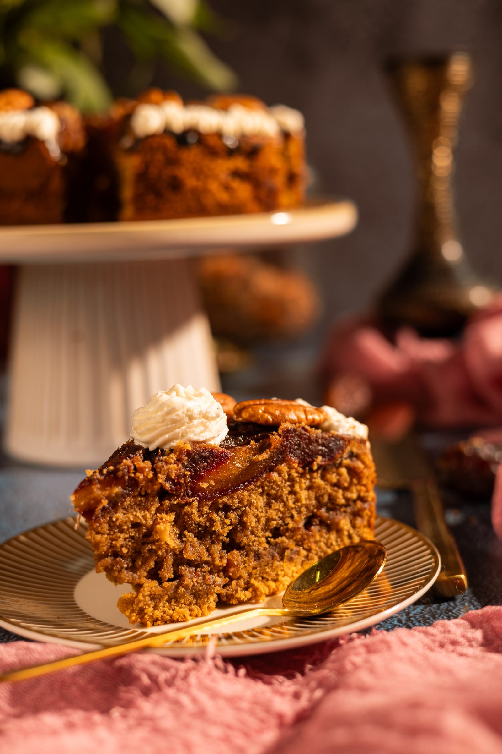 A slice of cake on a gold plate in front of the cake stand