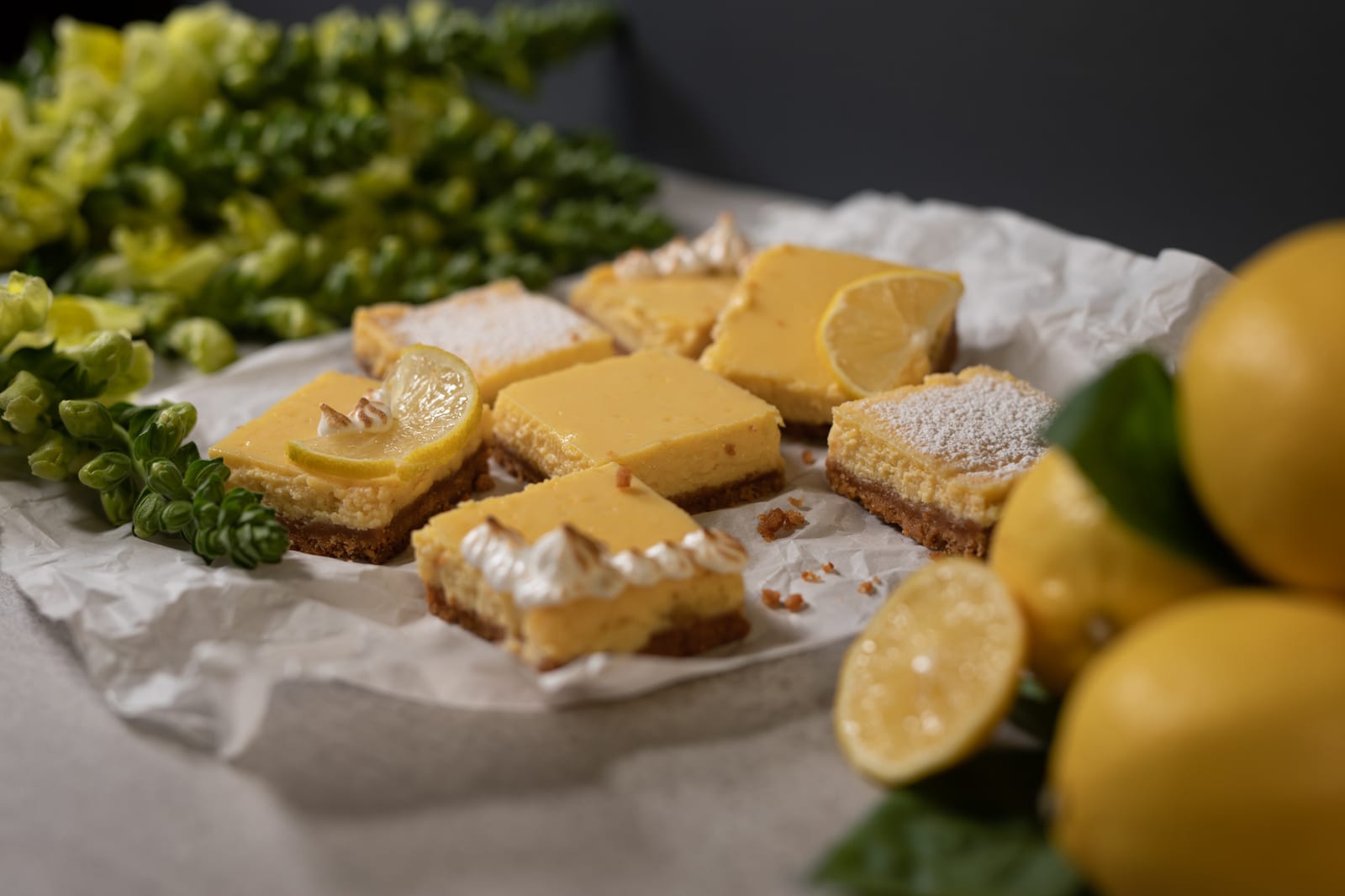 Sweet and tart lemon squares on parchment between snapdragons and lemons