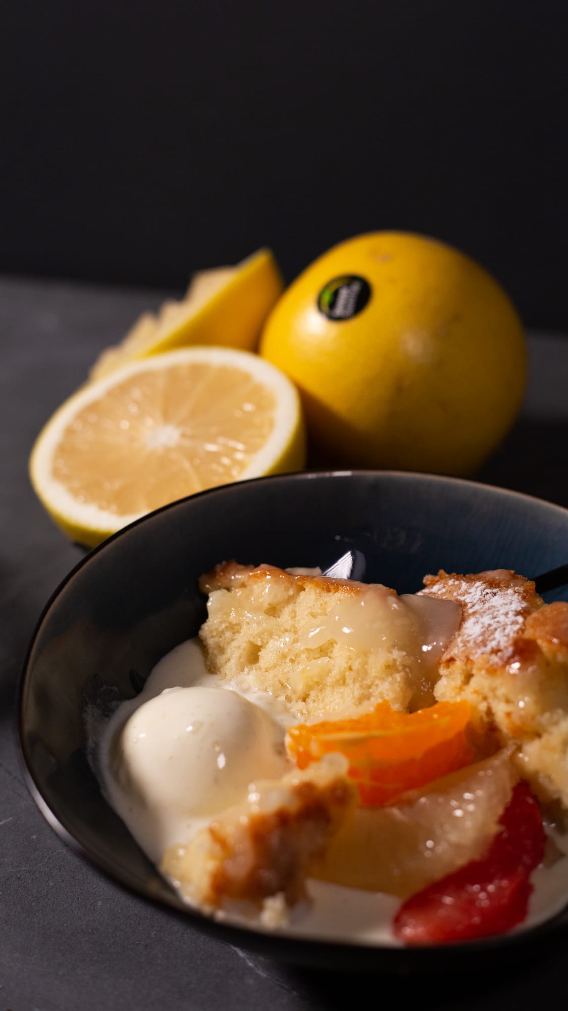 A bowl of pudding and sauce with a grapefruit behind