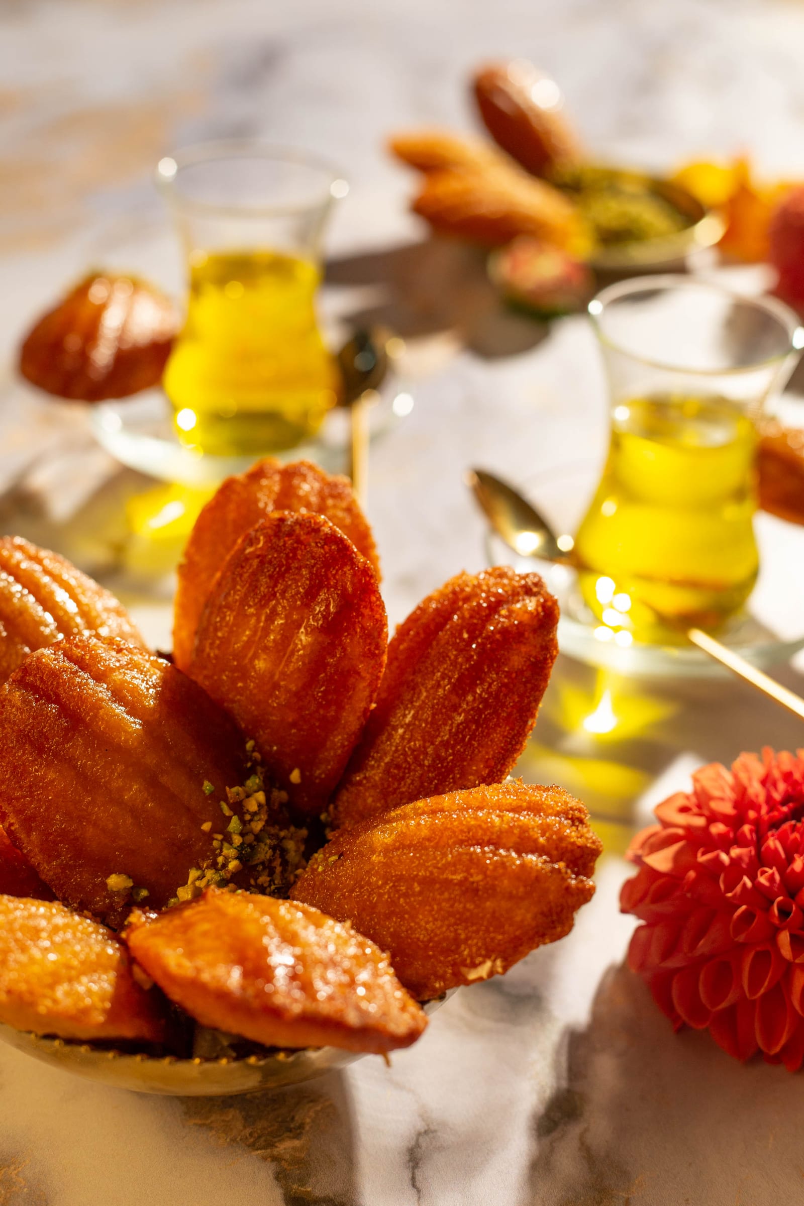 Orange blossom water madeleines arranged as petals in a gold dish, tea glasses behind