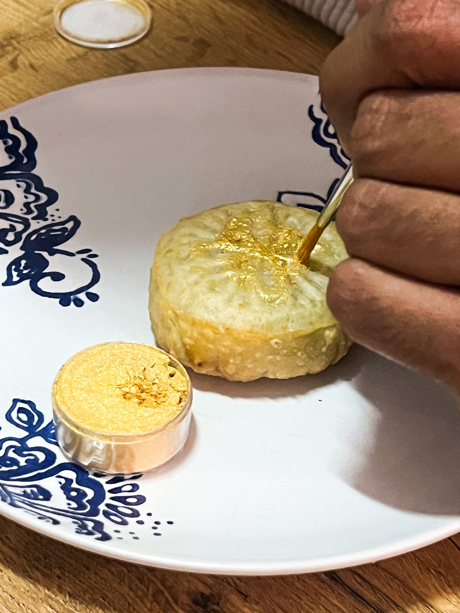 Brushing gold lustre onto a fried mawa ghari on a blue and white plate