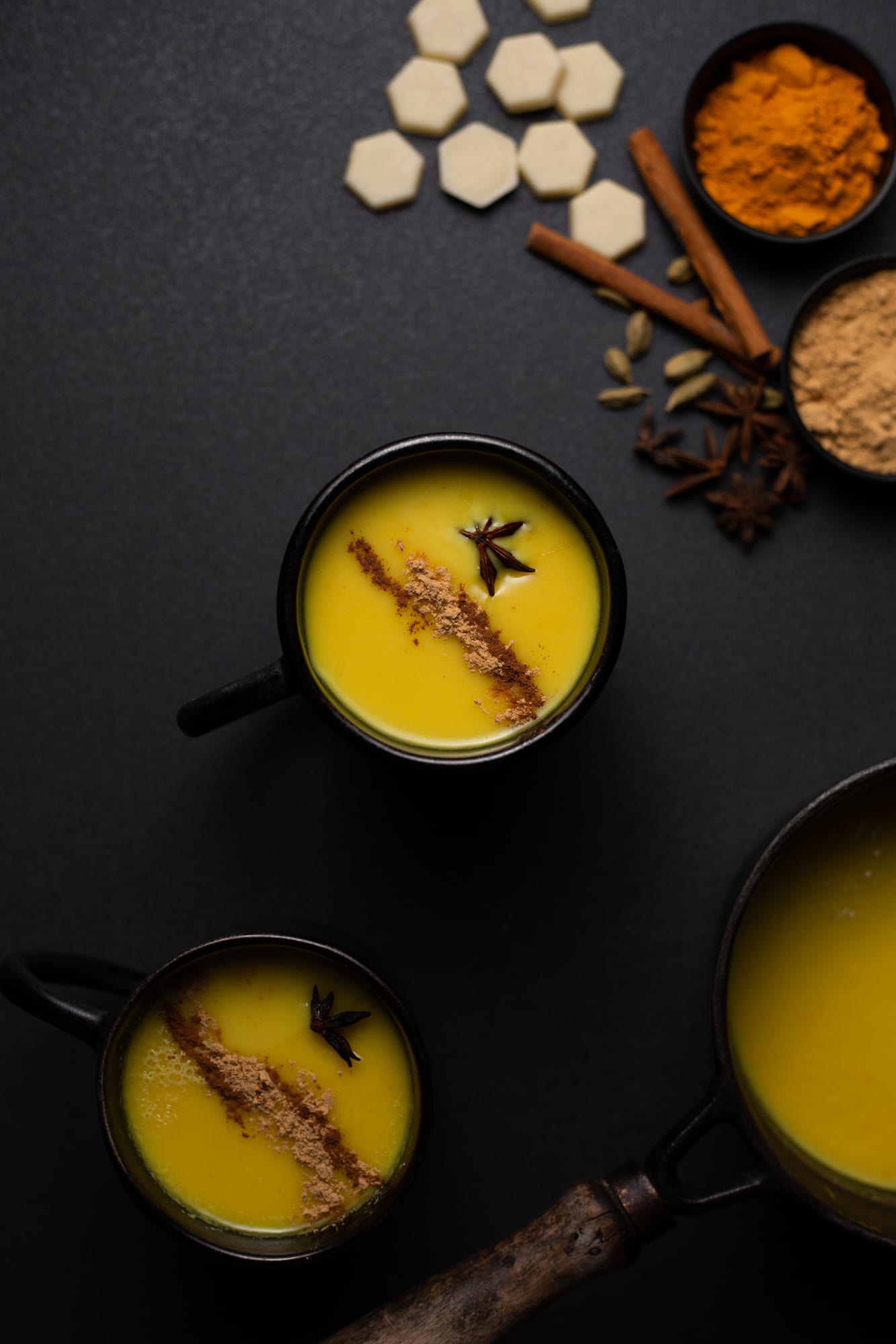 Mugs of golden turmeric and ginger white hot chocolate with cinnamon and star anise, from above