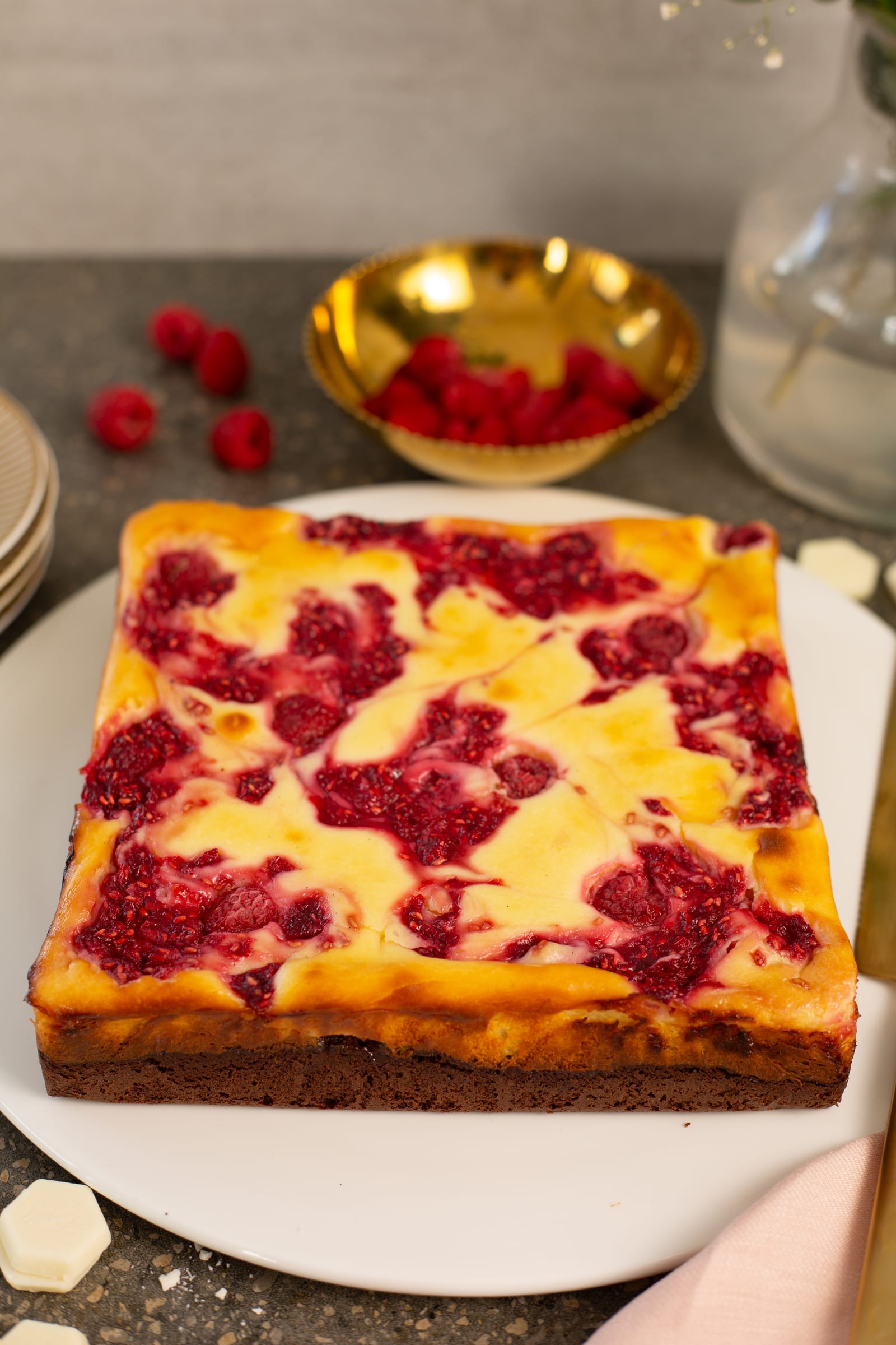 The whole raspberry ripple cheesecake brownie on a plate, with raspberries