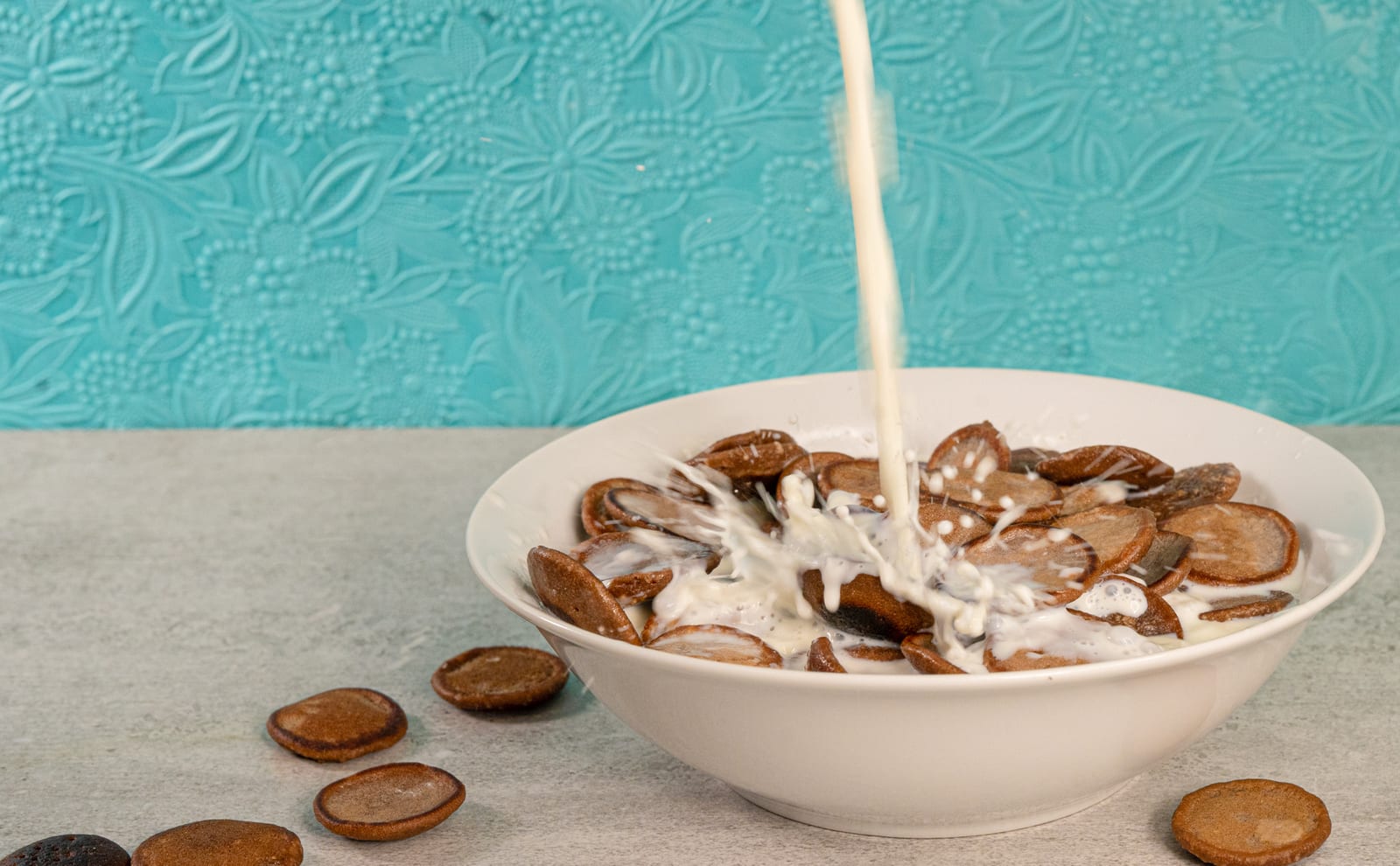 Milk splashing into a bowl of Milo pancake cereal, loose mini pancakes around it