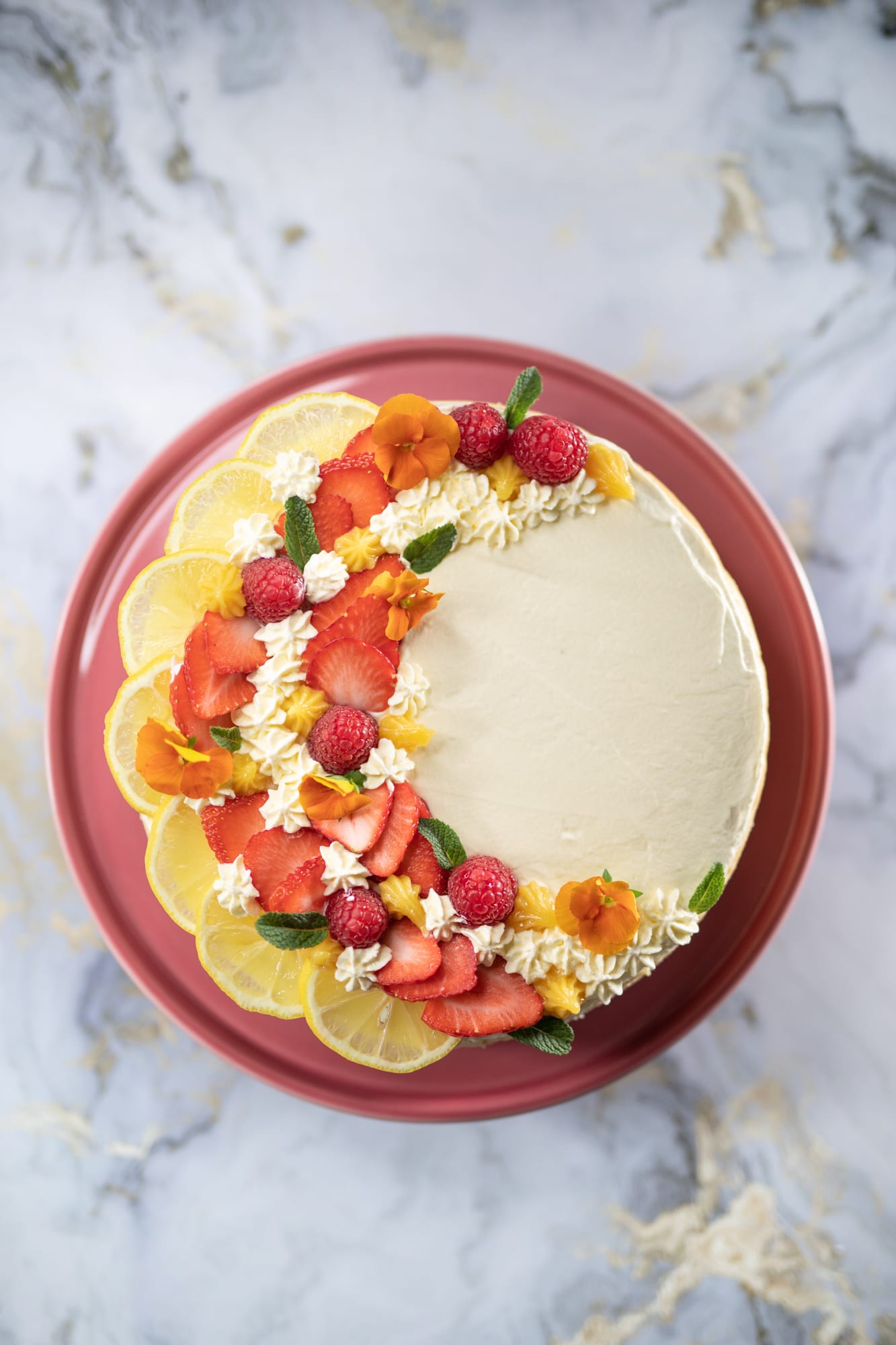 A whole creamy lemon cheesecake decorated with lemon slices, berries and flowers, from above
