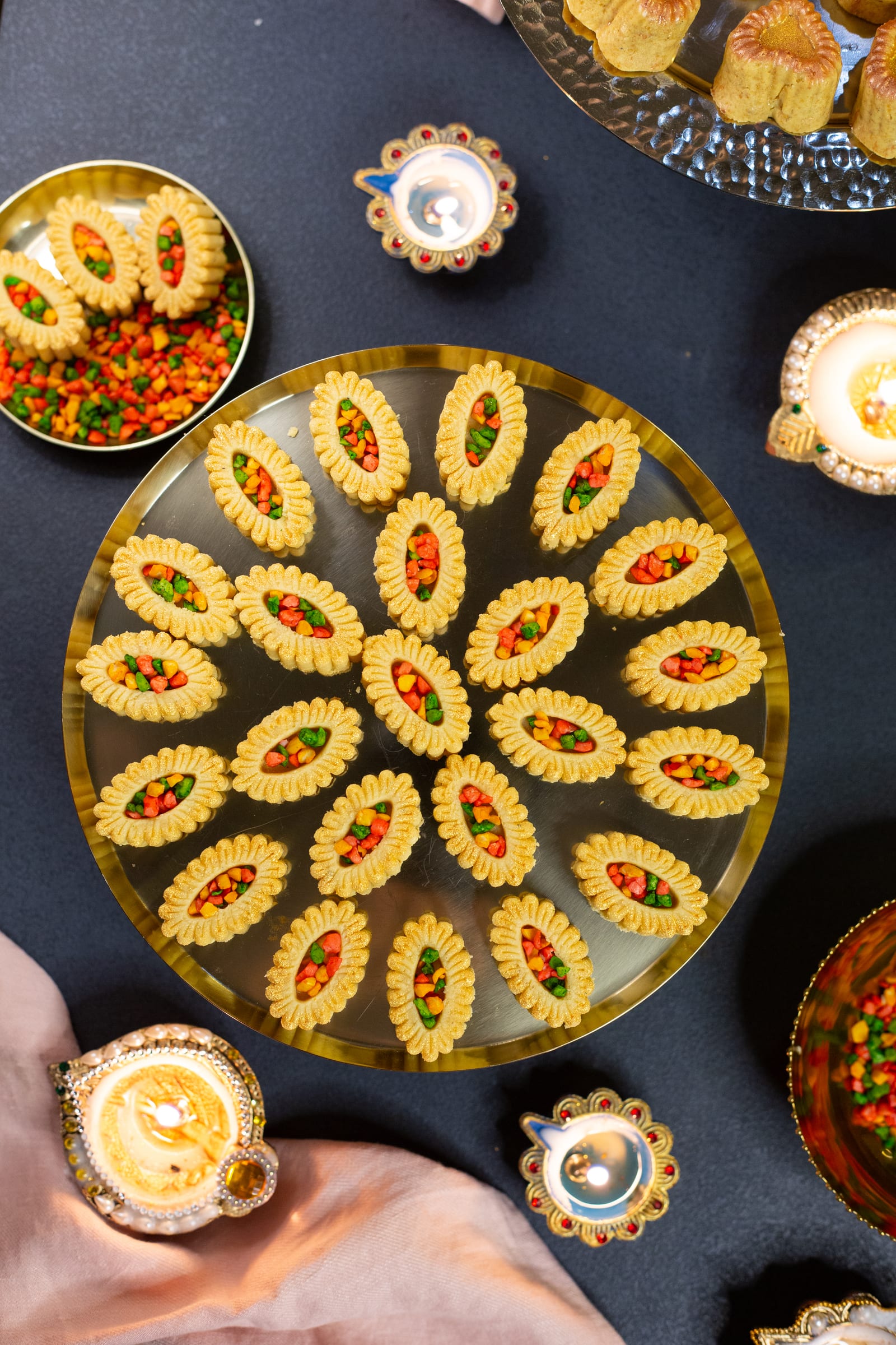 A platter of sweetmeats arranged in a flower pattern, with lit diyas