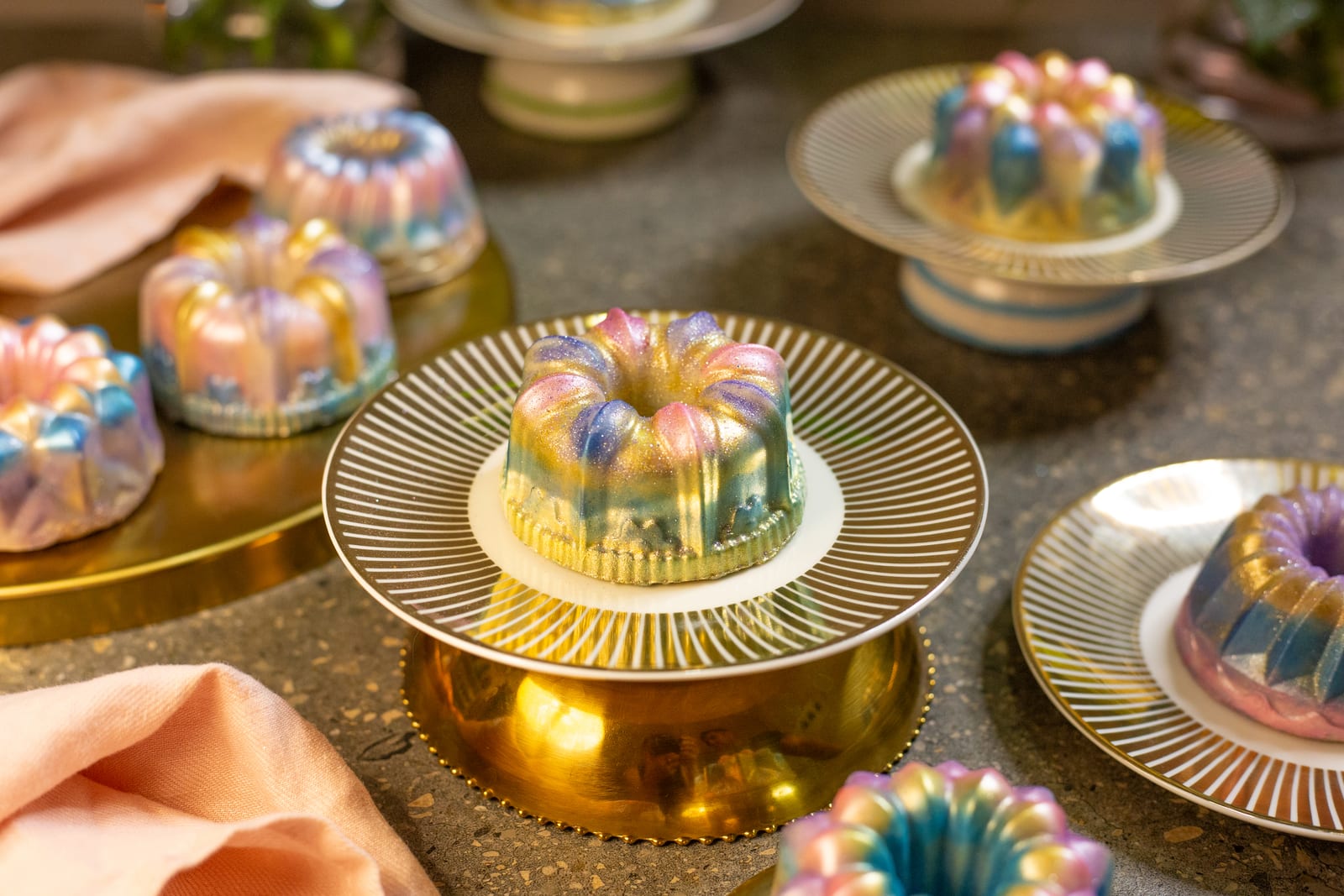 Dubai pistachio burfee bundts painted with lustre dust, one on a gold cake stand among the others on gold plates