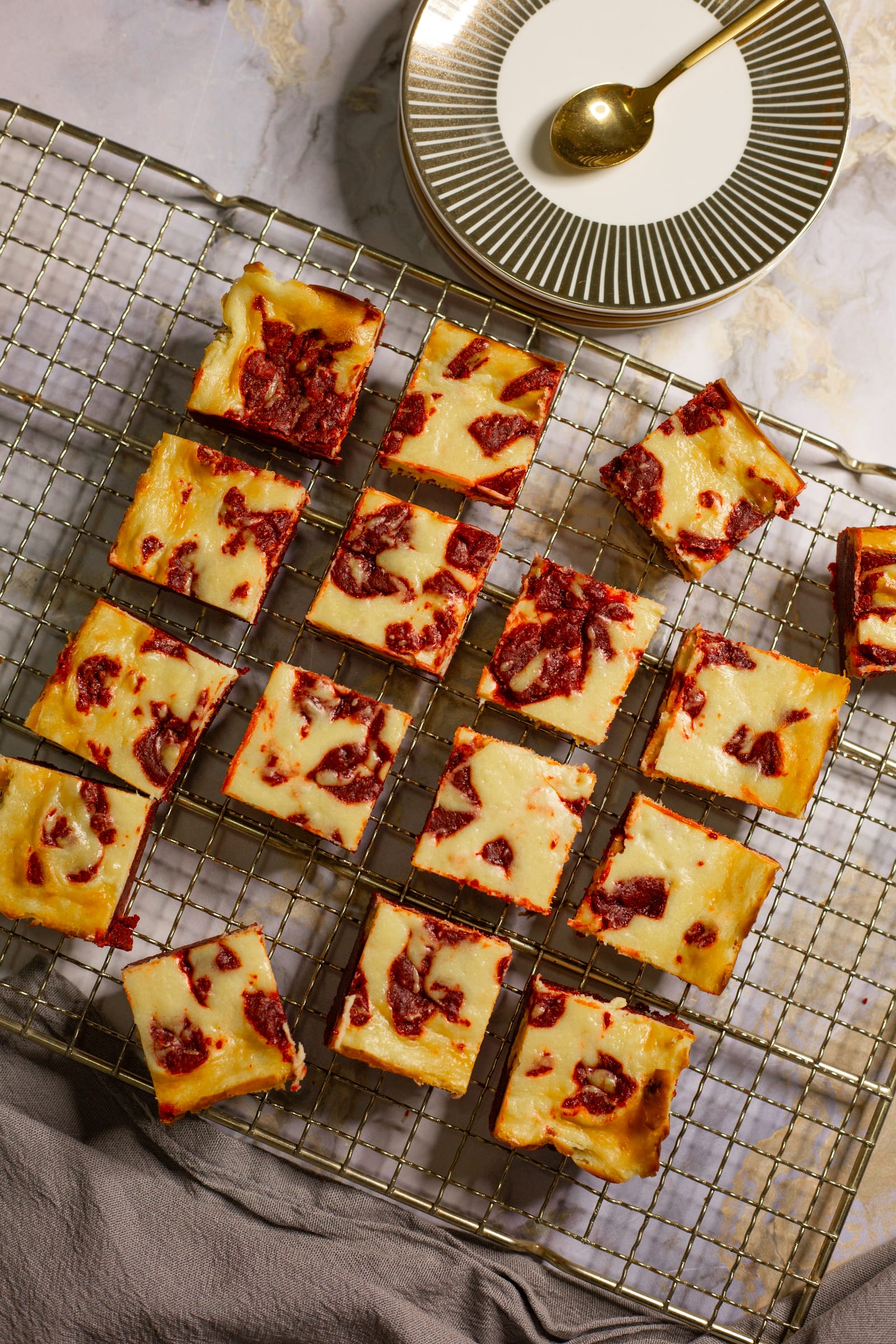 Squares of red velvet cheesecake blondies spread out on a cooling rack, from above