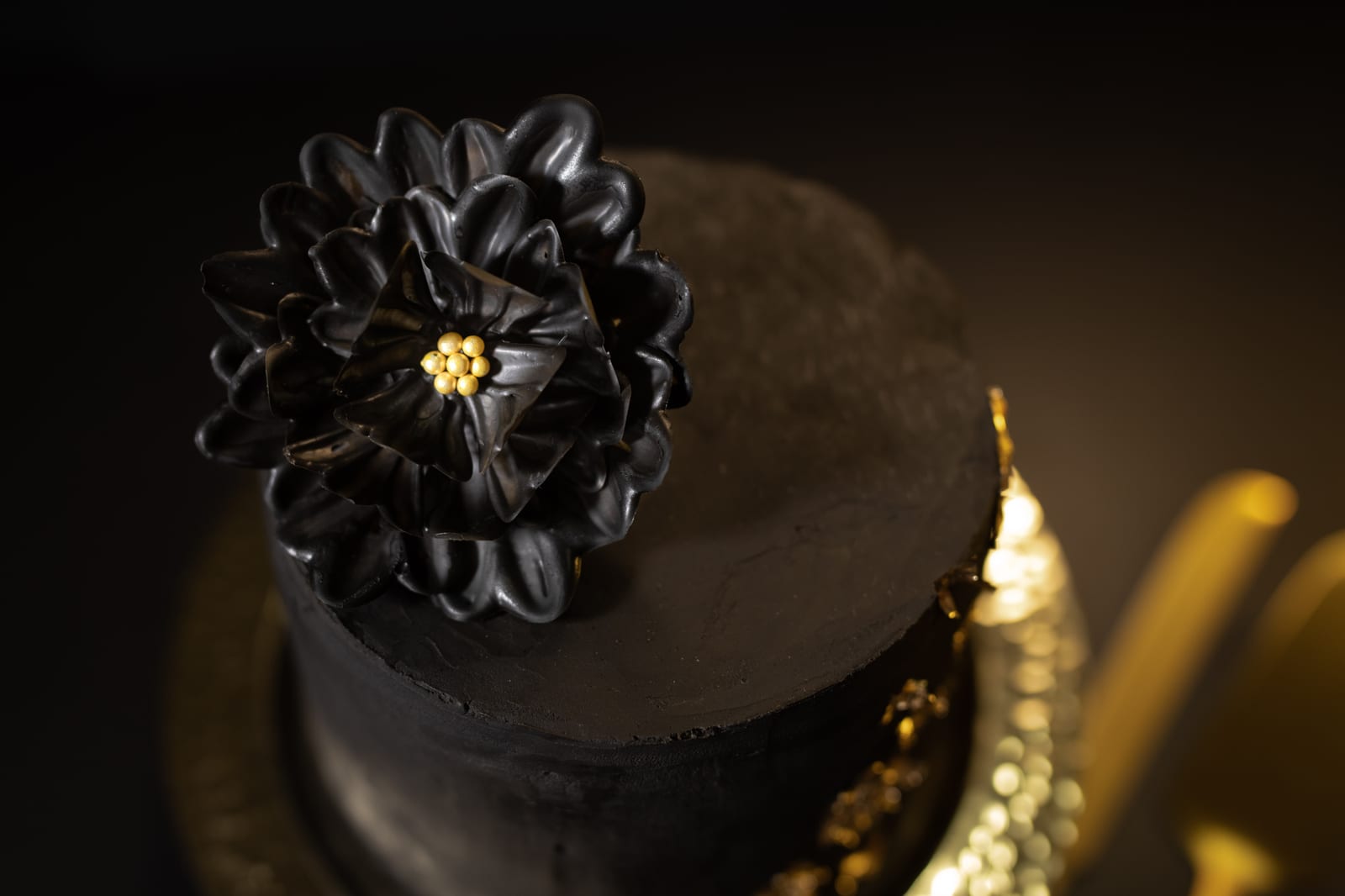 A black velvet cake topped with a dark chocolate flower on a hammered gold plate, gold cutlery beside it