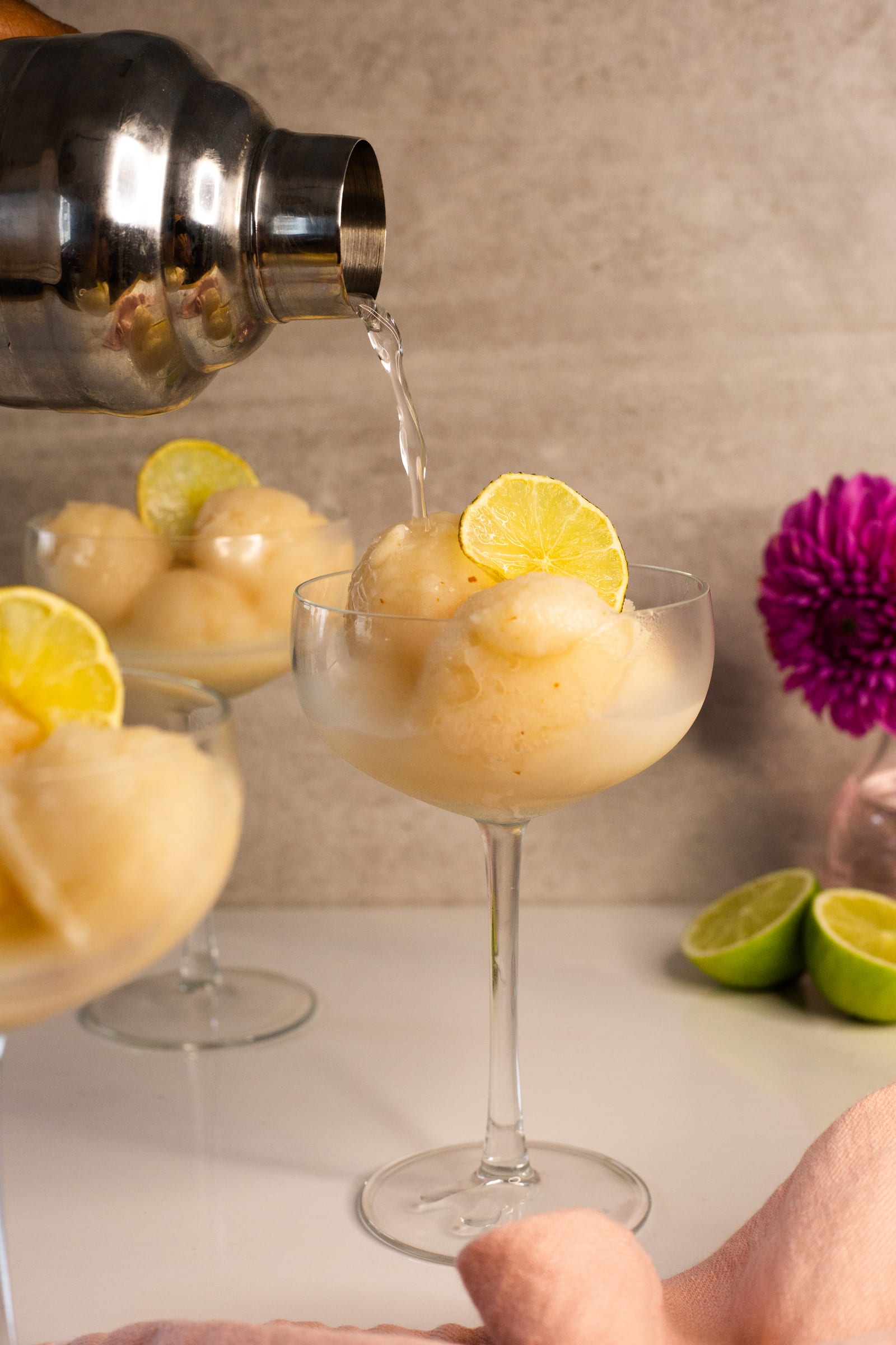 A cocktail shaker pouring over a coupe of litchi and lemon sorbet