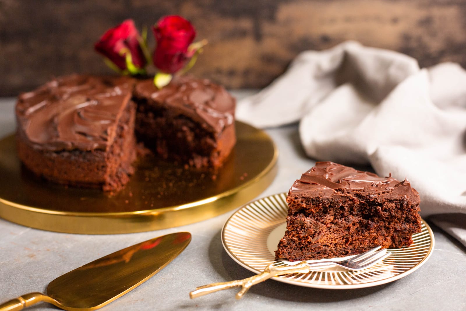 A slice of chocolate and beetroot cake on a gold-striped plate in front of the cut cake