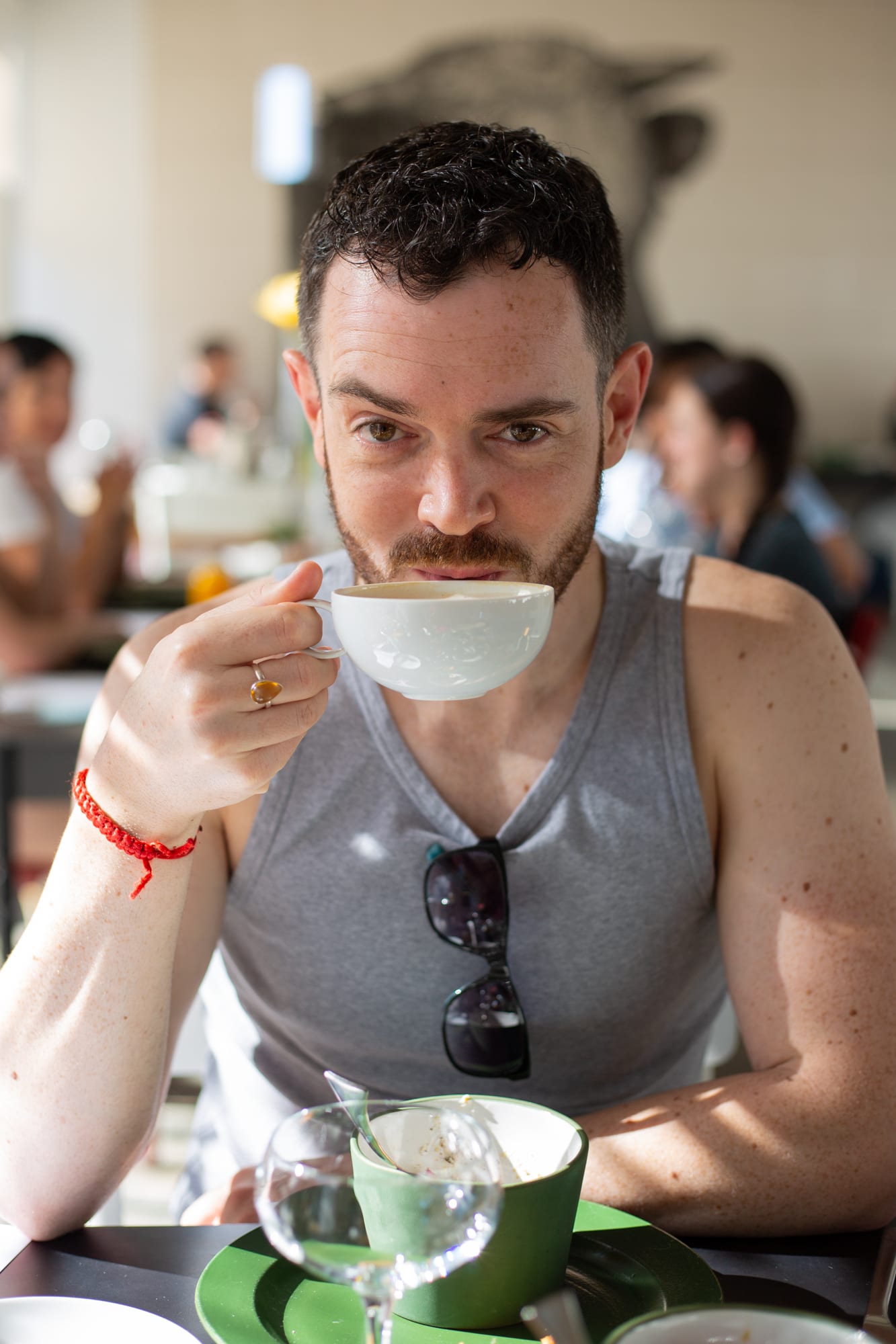 Linsen sipping a cappuccino at a breakfast table in Babel, with other diners blurred behind