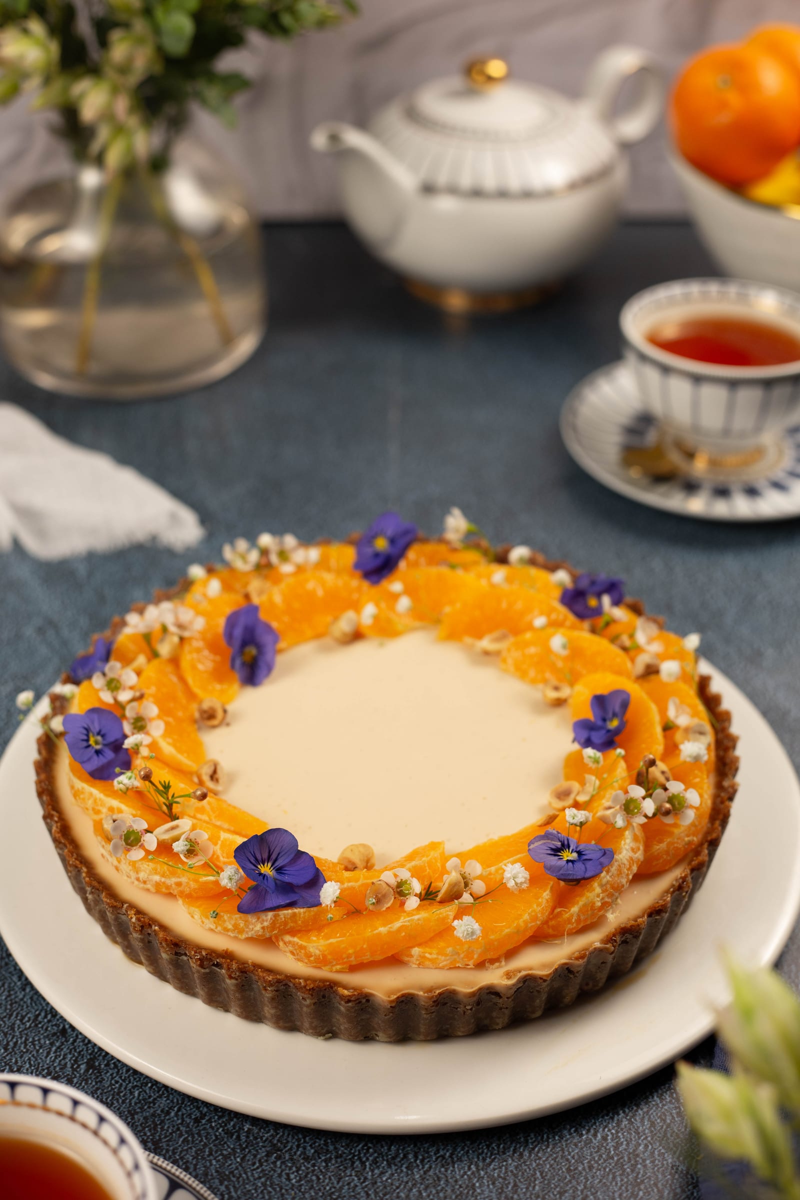 The panna cotta tart on a stand with a teapot and cups of rooibos behind