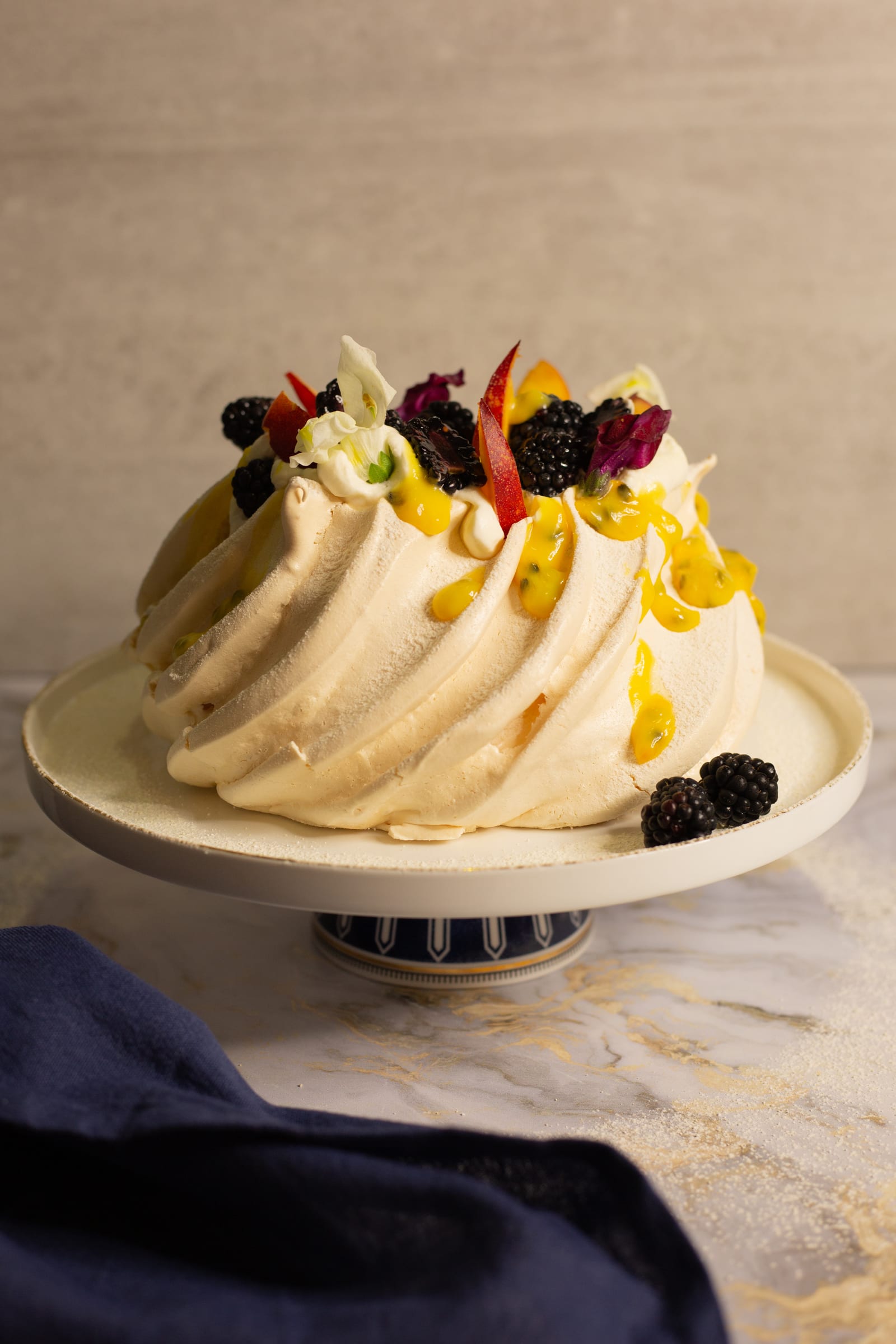 An earlier blackberry and nectarine pavlova on a cake stand, decorated with edible flowers