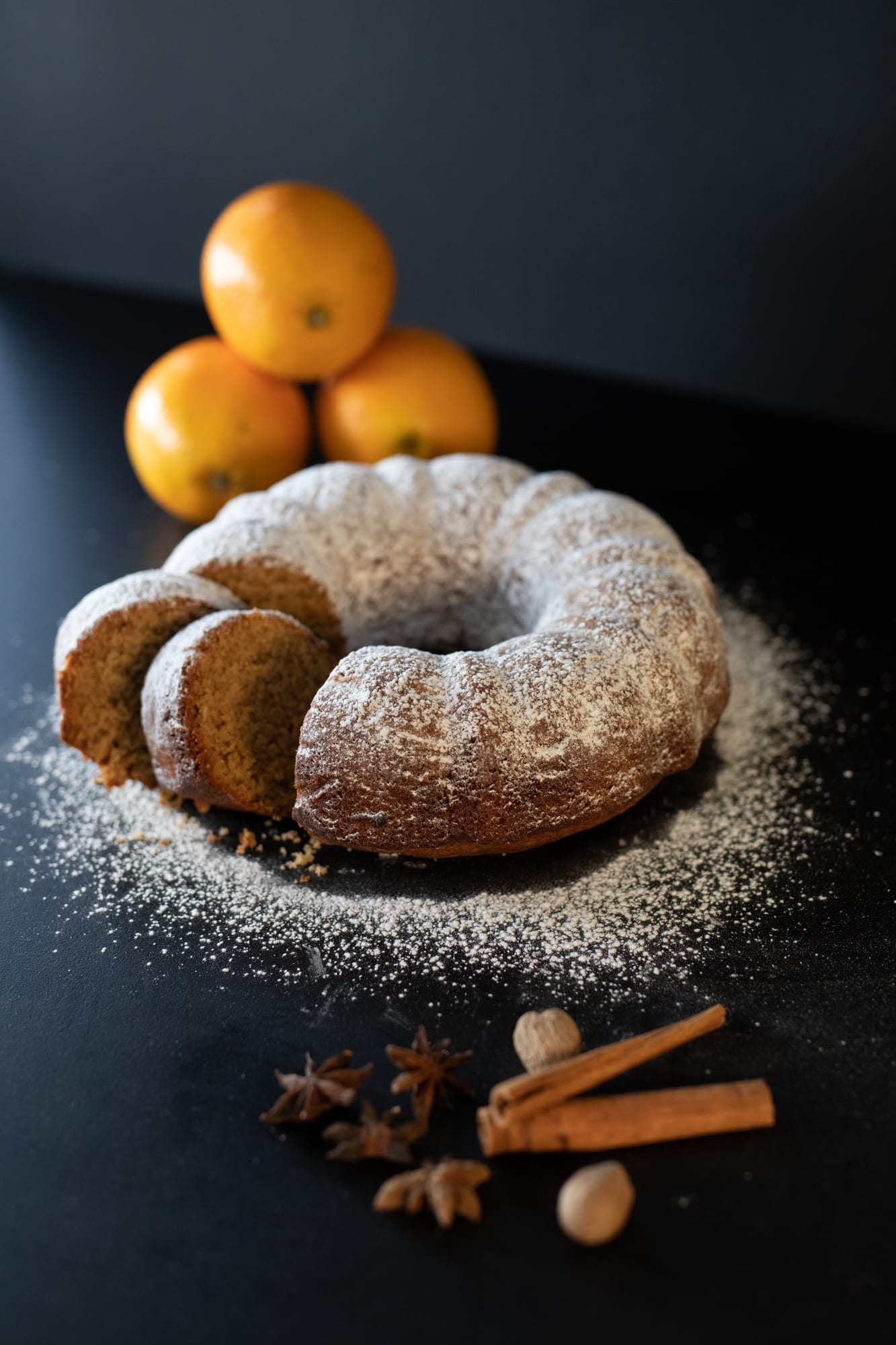 An orange spice pound cake with slices cut and leaning out, oranges behind