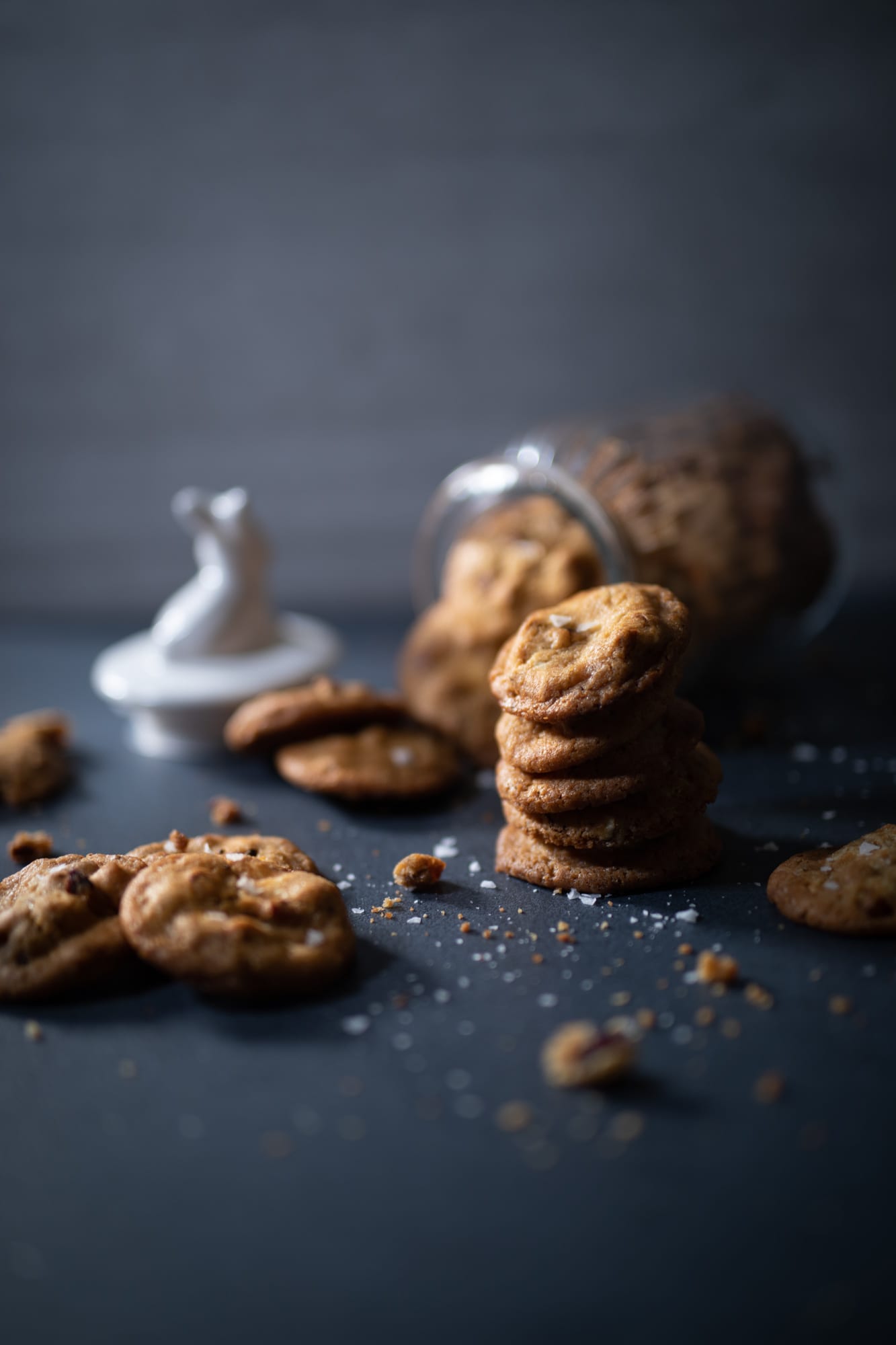 Pecan and white chocolate salted cookies spilling from a tipped jar, from a low angle