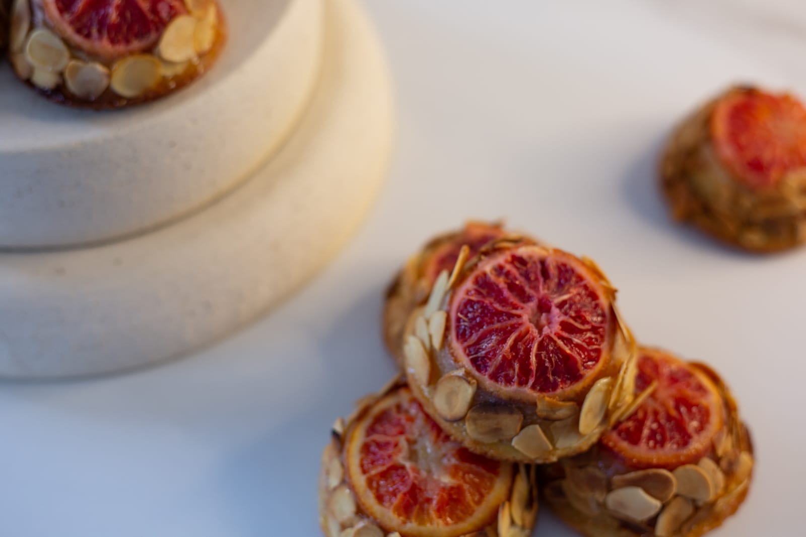 Blood orange and almond tea cakes stacked on white marble, a stone riser of more cakes behind