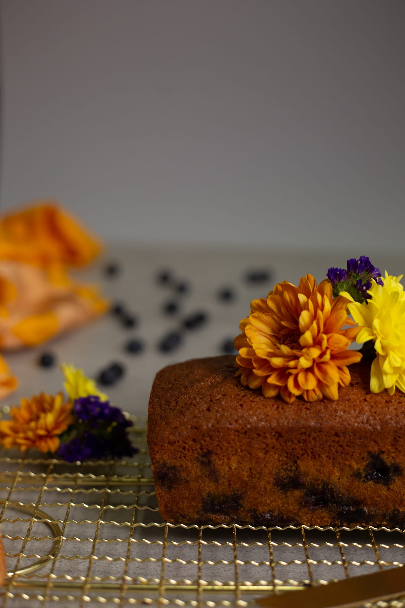 A whole lemon and blueberry loaf with flowers on top, blueberries scattered around