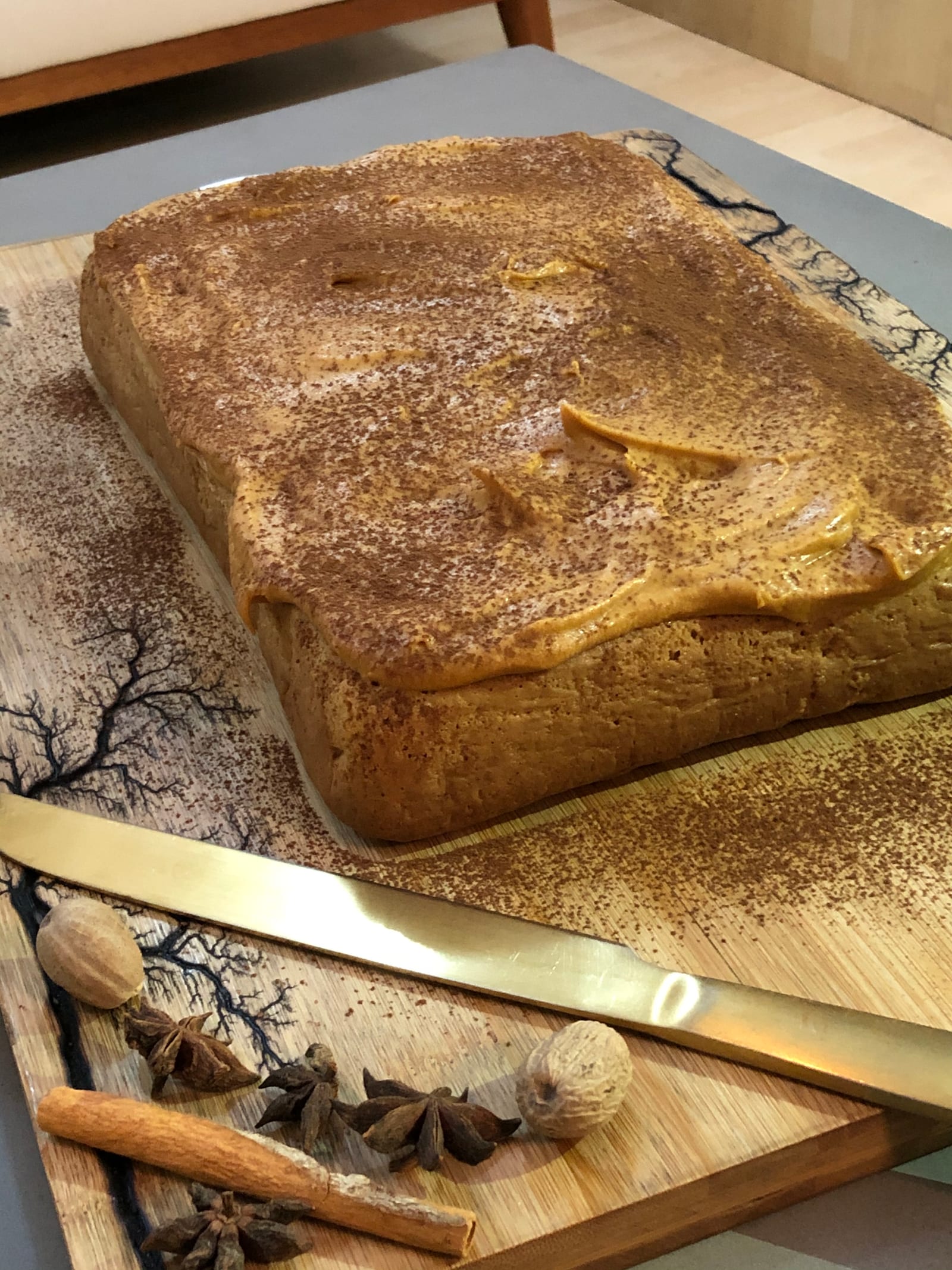 A masala tres leches cake on its board with a gold knife and spices, from slightly above