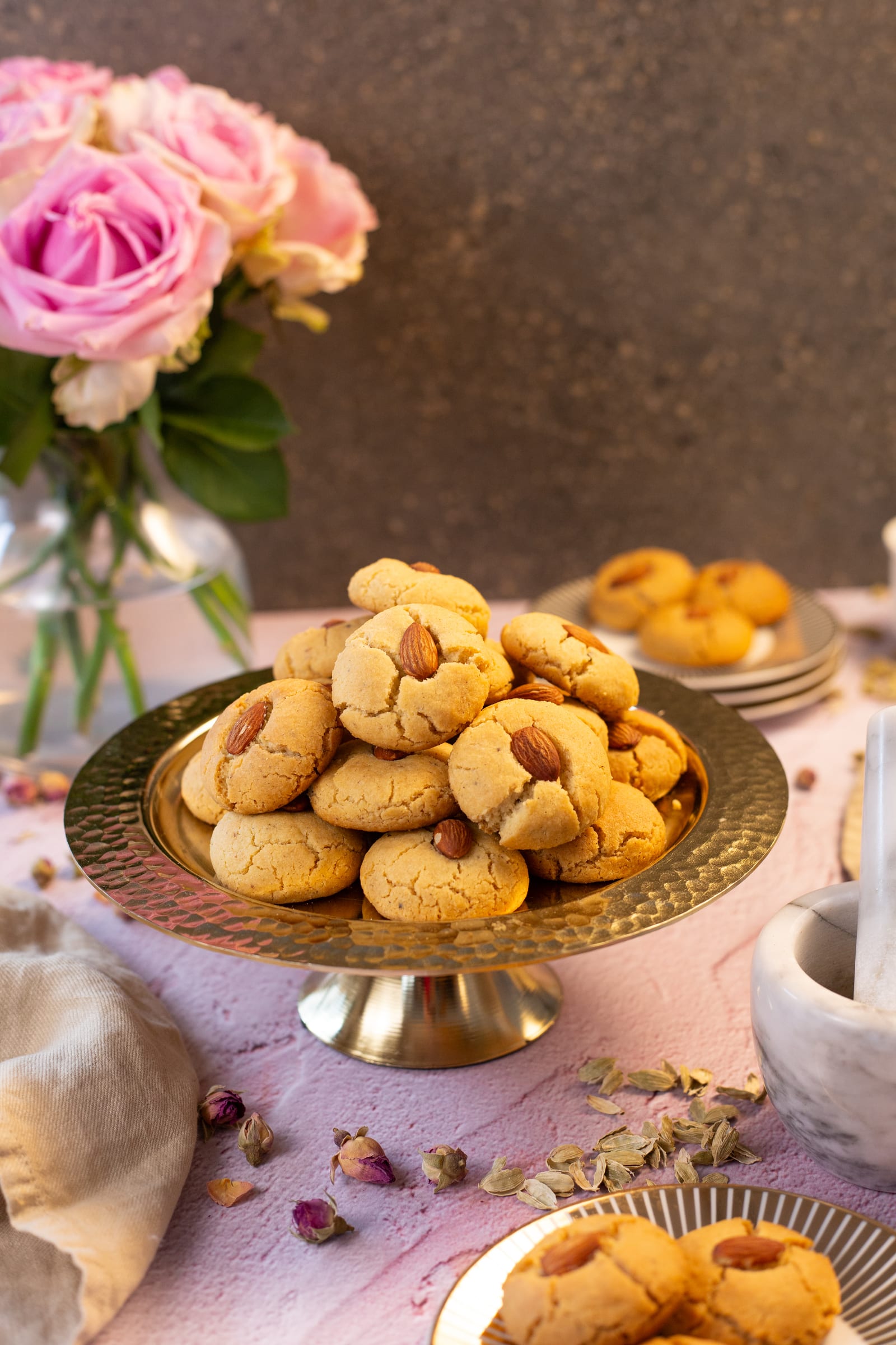 Naan kathai on a brass cake stand, with pink roses and a pestle and mortar