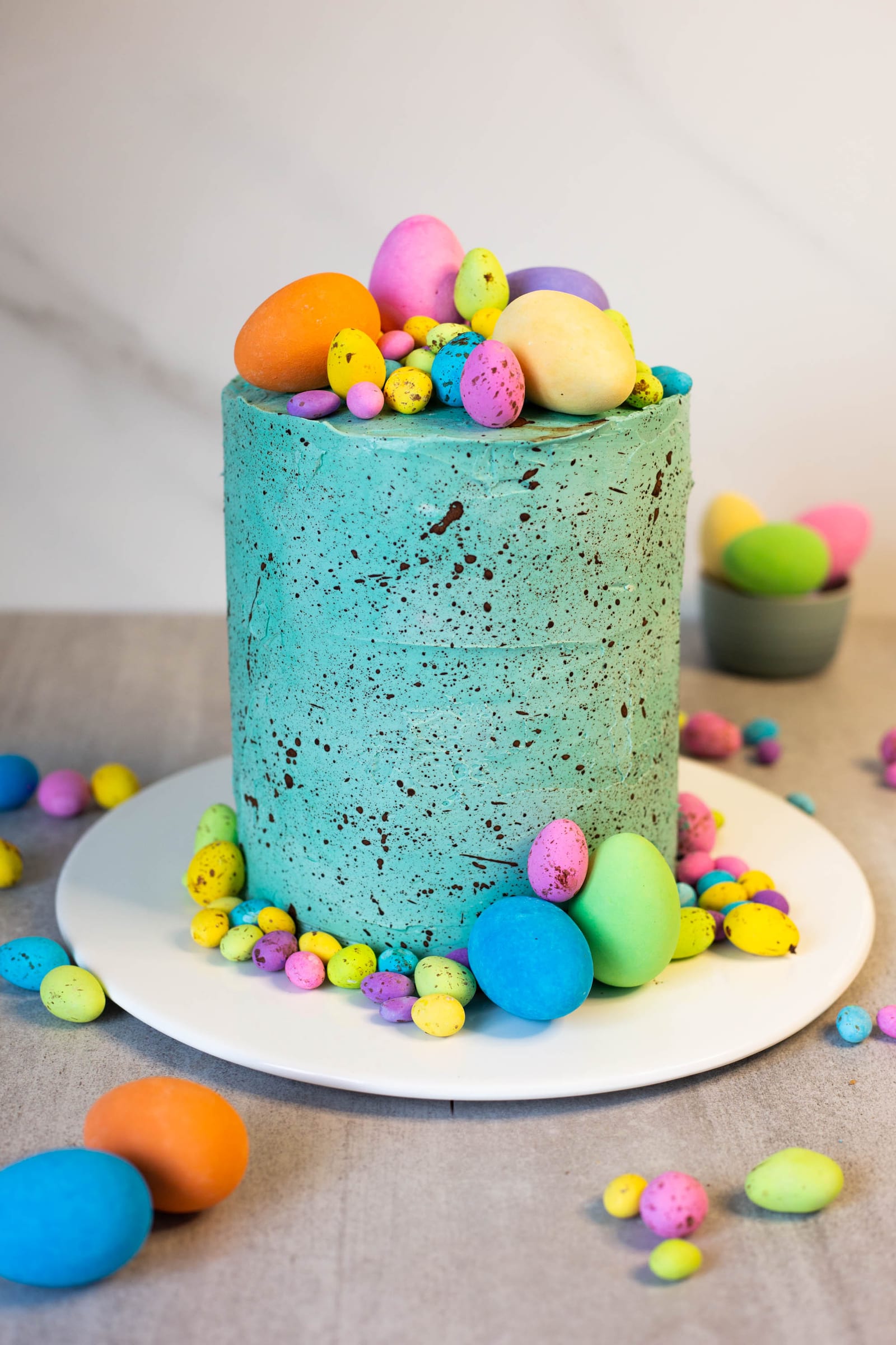 A tall speckled egg cake covered in duck egg blue buttercream and topped with speckled eggs