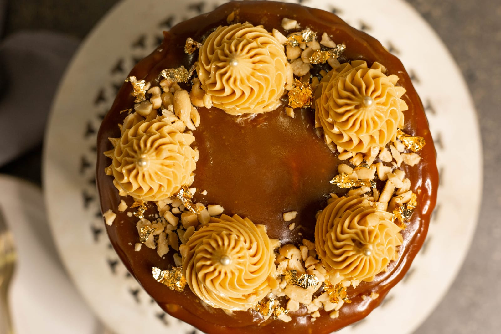 The top of a salted caramel peanut cake with caramel, piped rosettes and chopped peanuts, from above