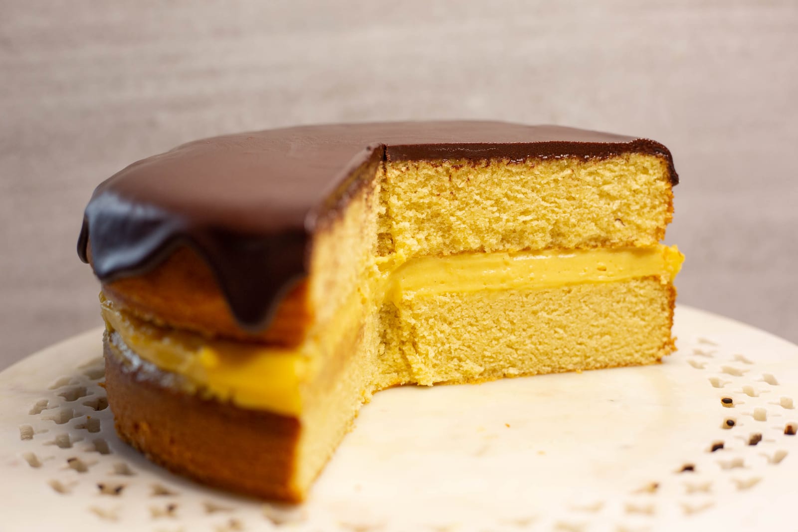 A cut Boston cream pie showing layers of vanilla sponge, thick custard and dark chocolate ganache