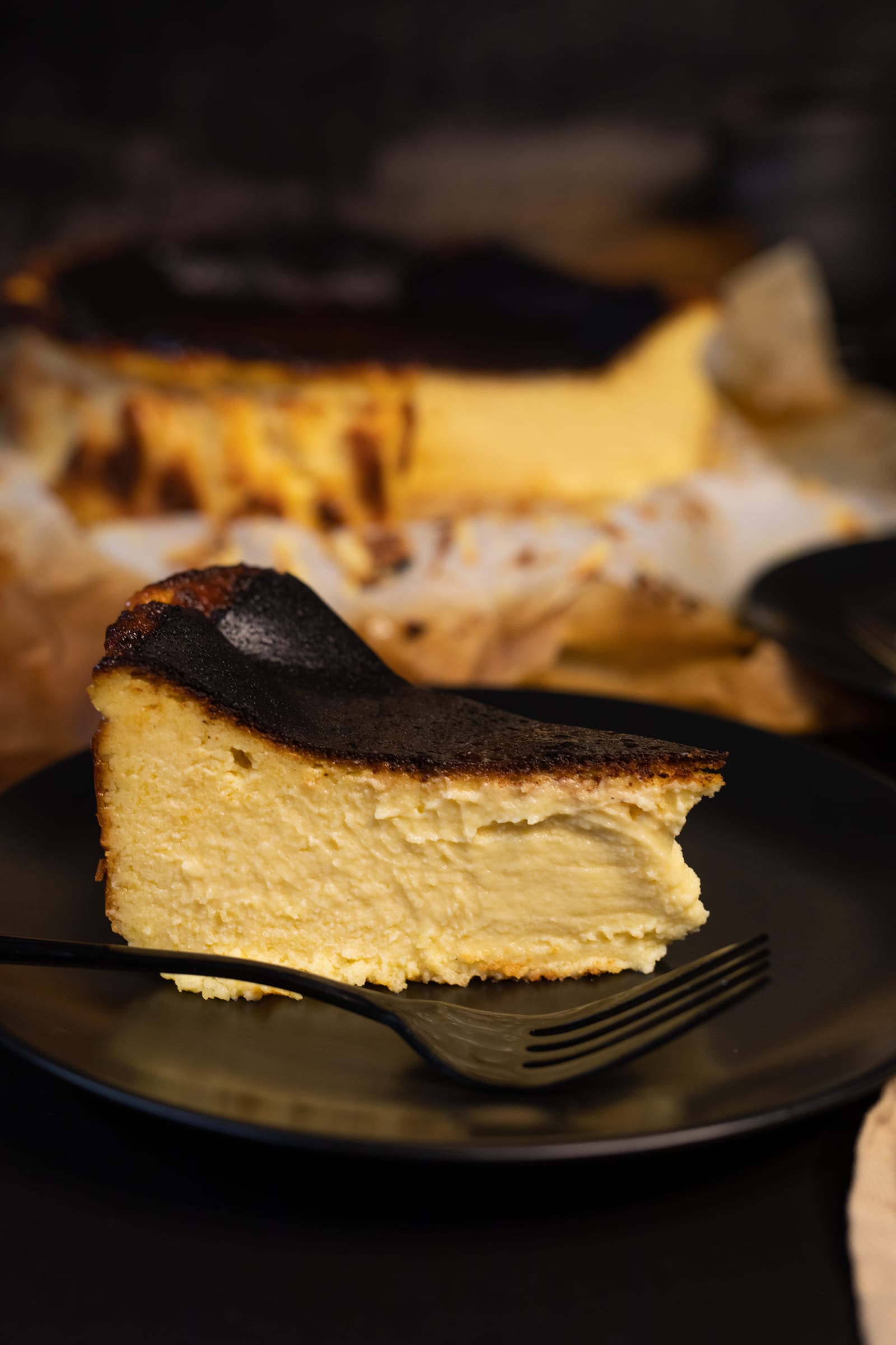 A slice of Basque cheesecake on a dark plate, showing its creamy custardy centre